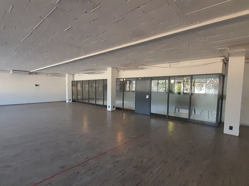 Spacious open-plan office area featuring exposed concrete ceilings, modern glass partitioning, and durable laminate flooring, offering a versatile workspace layout.