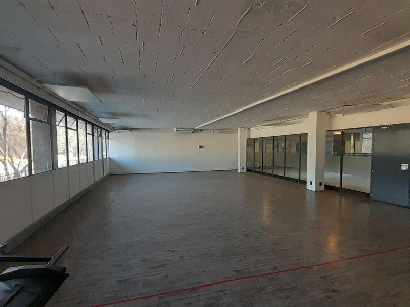 Spacious open-plan office area featuring exposed concrete ceilings, large windows for natural light, and glass partition walls.