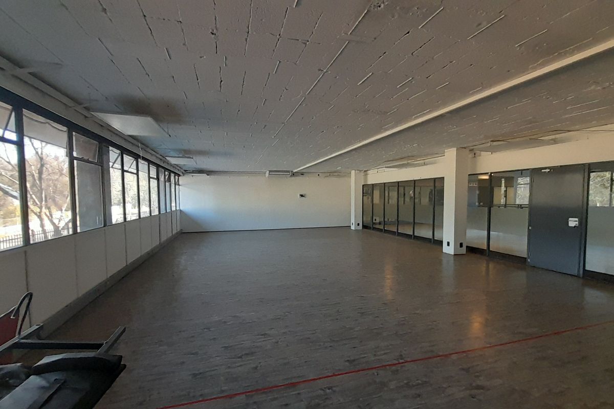 Spacious open-plan office area featuring exposed concrete ceilings, large windows for natural light, and glass partition walls.