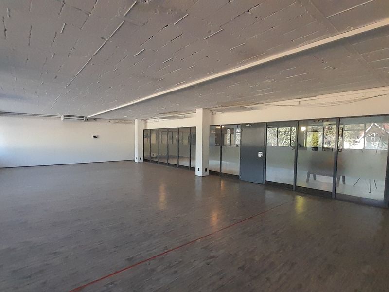 A spacious, open-plan office area featuring exposed concrete ceilings, laminate flooring, and glass partition walls, offering a versatile workspace layout.