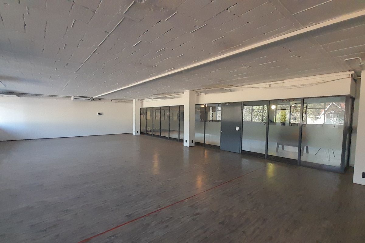 A spacious, open-plan office area featuring exposed concrete ceilings, laminate flooring, and glass partition walls, offering a versatile workspace layout.