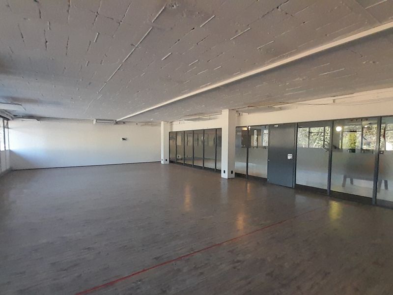 Spacious open-plan office area featuring exposed concrete ceilings, large windows for natural light, and glass partition walls.