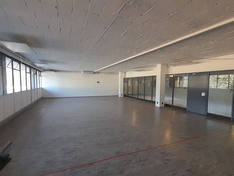 Spacious open-plan office area featuring exposed concrete ceilings, large windows for natural light, and glass partition walls, offering a versatile workspace.