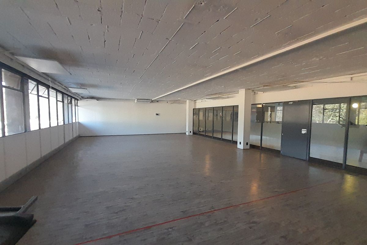 Spacious open-plan office area featuring exposed concrete ceilings, large windows for natural light, and glass partition walls, offering a versatile workspace.