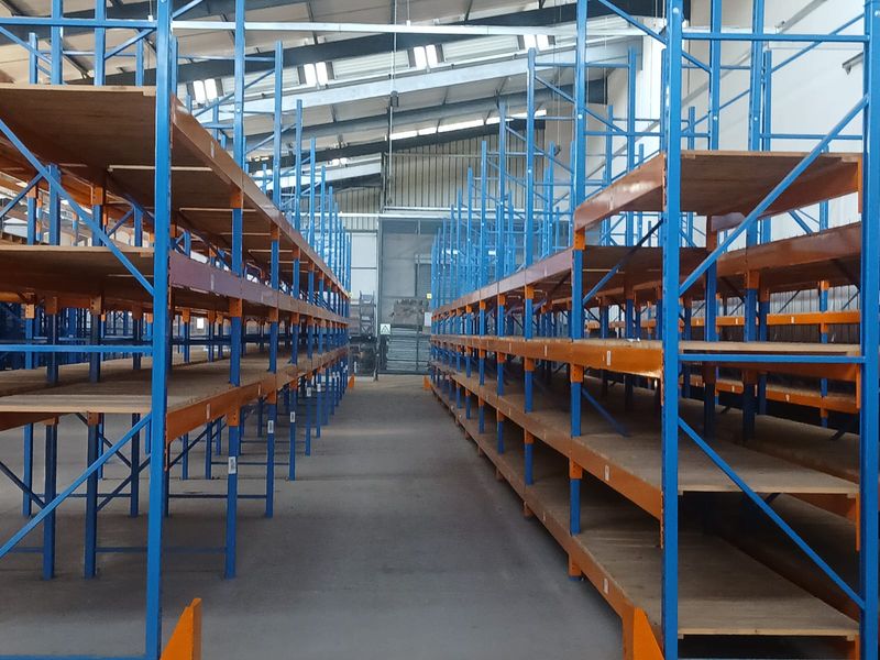 Spacious industrial warehouse interior featuring extensive fixed steel racking systems, concrete flooring, and high-clearance roof structure with integrated skylights.