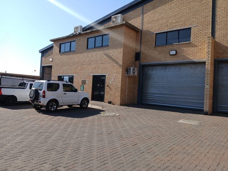 Industrial property exterior featuring a face brick facade, roller shutter door, paved driveway, and wall-mounted air conditioning units.