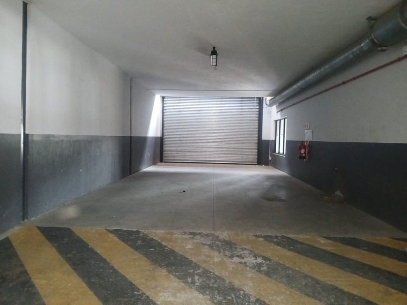 Spacious industrial garage featuring a roller shutter door, exposed ventilation ducting, and durable concrete flooring, suitable for storage or vehicle access.