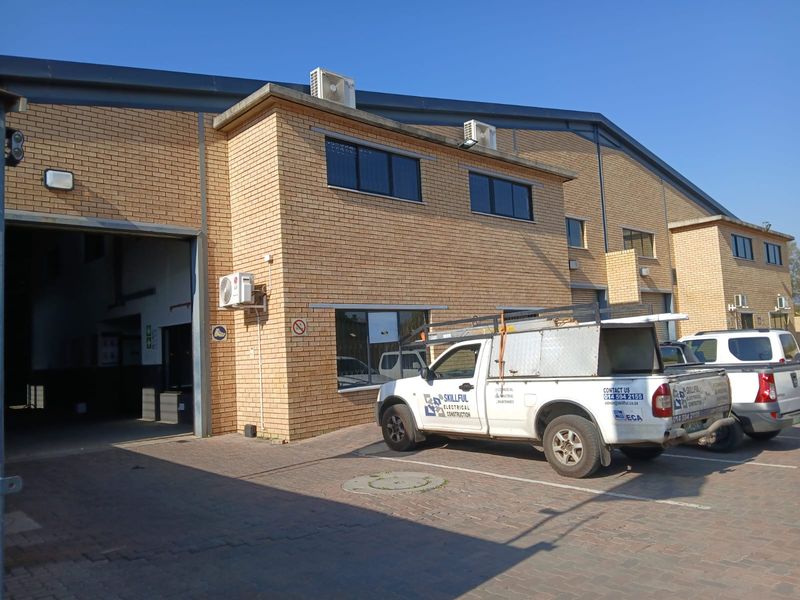 Front elevation of an industrial warehouse facility featuring face brick construction, large roller shutter access, and paved parking area.