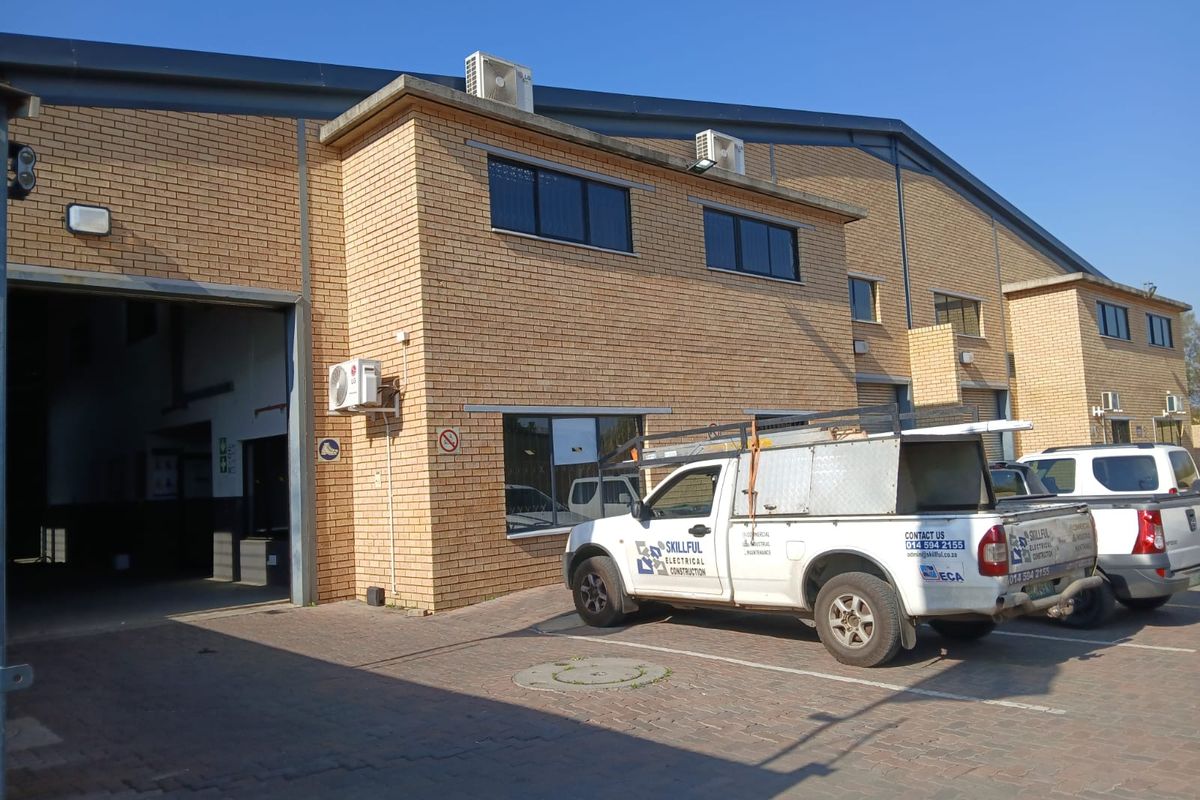 Front elevation of an industrial warehouse facility featuring face brick construction, large roller shutter access, and paved parking area.