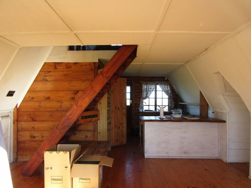 Open plan living area featuring timber wall paneling, wooden flooring, a staircase, and a functional kitchen counter space in a rustic farm setting.