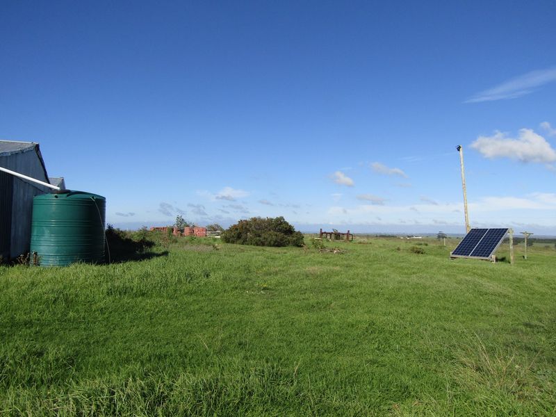 Open farm land featuring a large green water storage tank and a ground-mounted solar panel array.