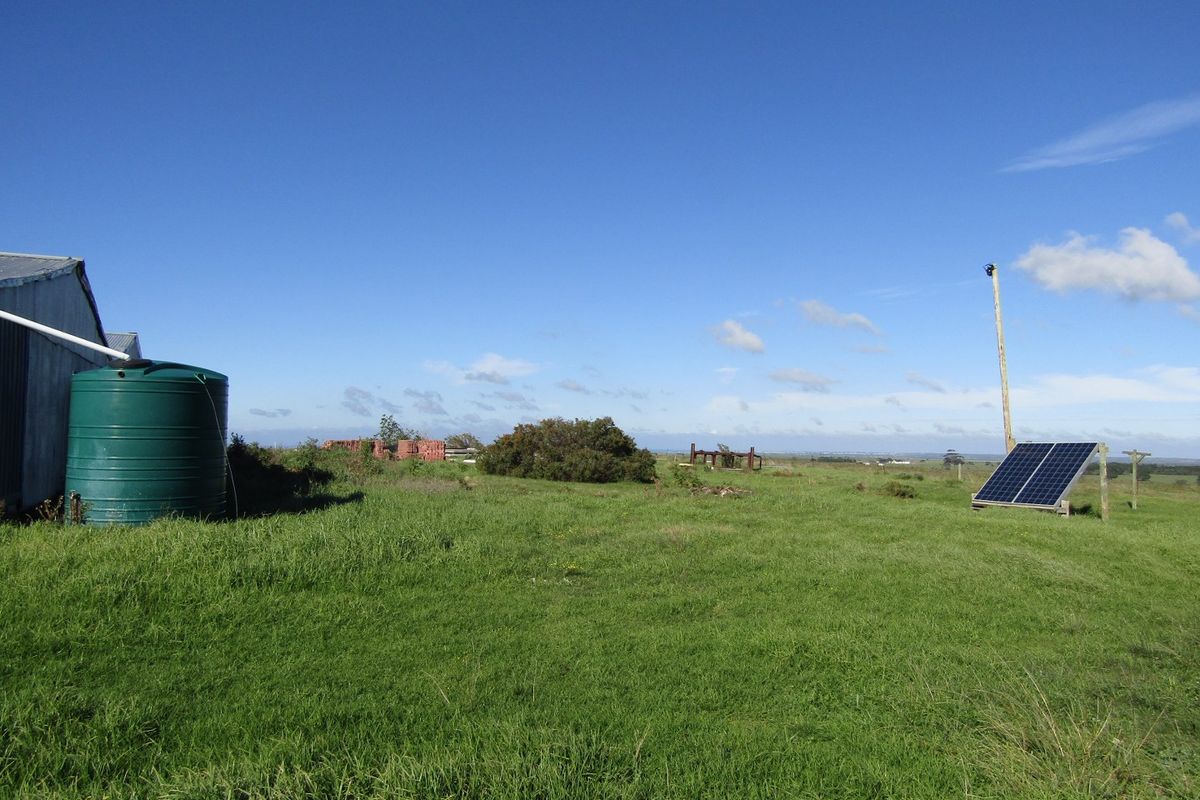 Open farm land featuring a large green water storage tank and a ground-mounted solar panel array.