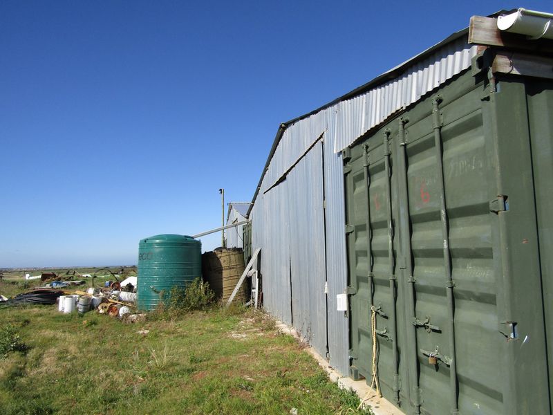 Exterior view of a farm outbuilding featuring corrugated metal siding and an integrated shipping container, with an adjacent water storage tank.