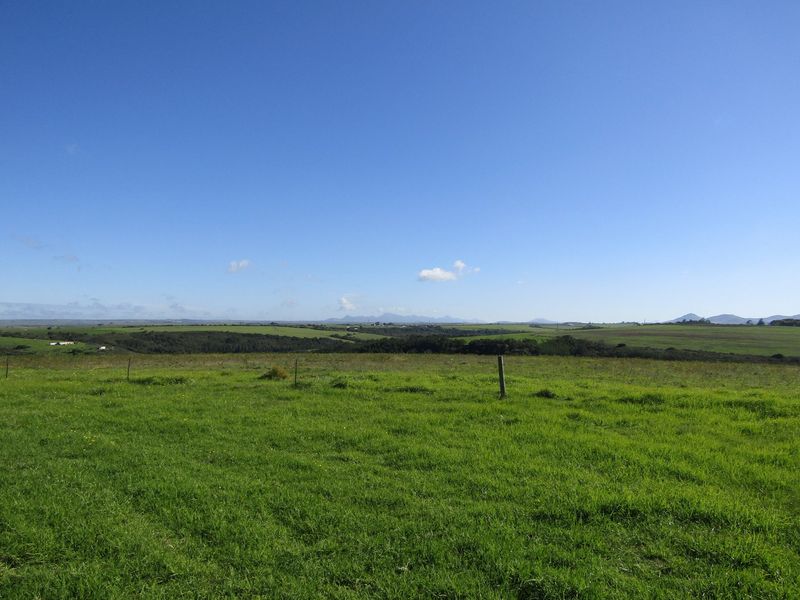 Expansive rural landscape view featuring rolling green pastures and distant mountain ranges under a clear blue sky.