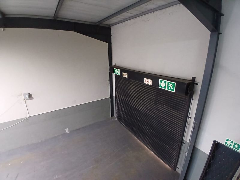 A functional utility or storage area featuring a large roller shutter door, exposed steel structural elements, and clear emergency exit signage.