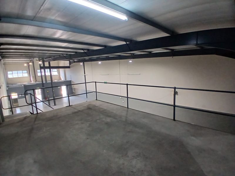Spacious mezzanine level in a retail or industrial unit featuring exposed steel beams, concrete flooring, and safety railings, suitable for storage or office conversion.