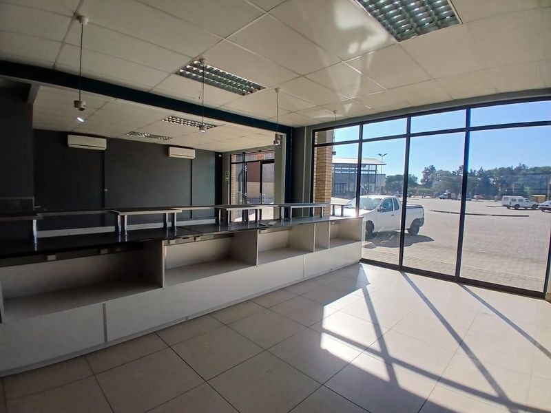 Spacious open-plan retail area featuring large glass storefront windows, tiled flooring, built-in service counter, and split-system air conditioning units.