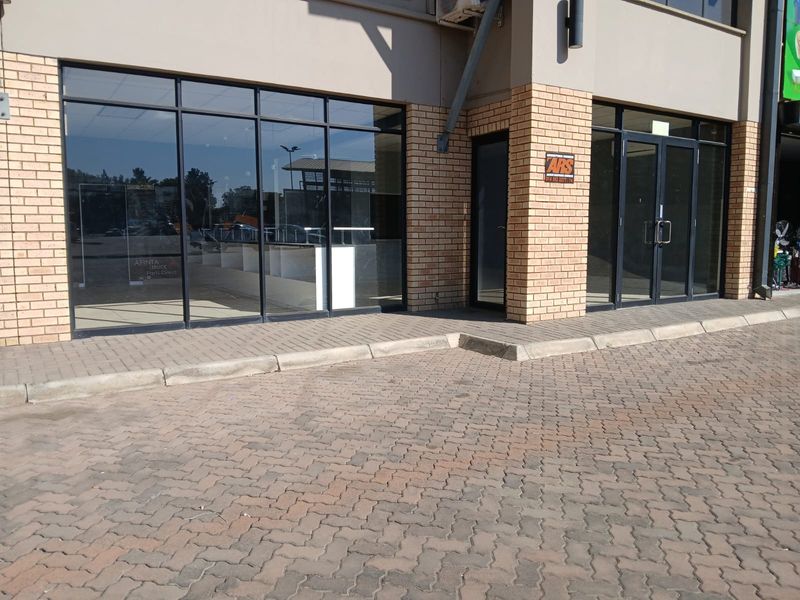 Front exterior view of a retail storefront featuring large glass windows, double entrance doors, and a paved parking area.