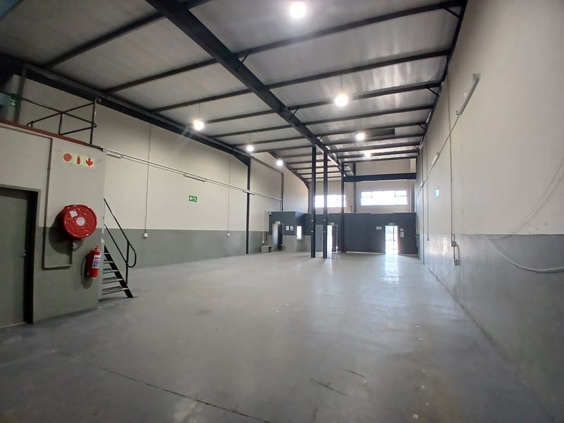 Spacious industrial warehouse unit featuring high ceilings, exposed steel structural beams, concrete flooring, and integrated fire safety equipment.