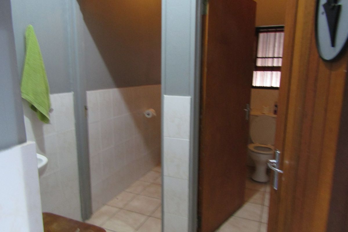 A functional bathroom featuring tiled flooring, wall tiling, a toilet, and a washbasin, with wooden door access.