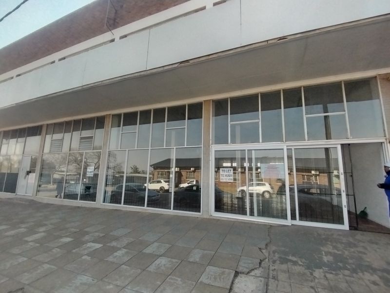 Front exterior view of a retail property featuring large glass storefront windows, sliding entrance doors, and a paved walkway area.