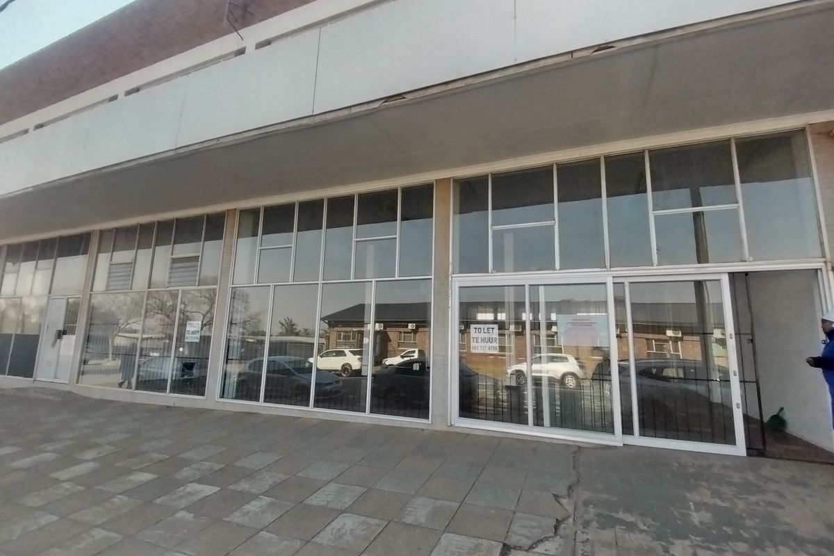 Front exterior view of a retail property featuring large glass storefront windows, sliding entrance doors, and a paved walkway area.