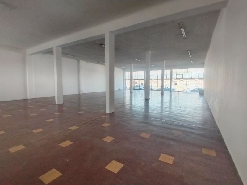 A spacious, open-plan retail unit featuring structural columns, large display windows for natural light, and durable tiled flooring, suitable for various commercial business applications.
