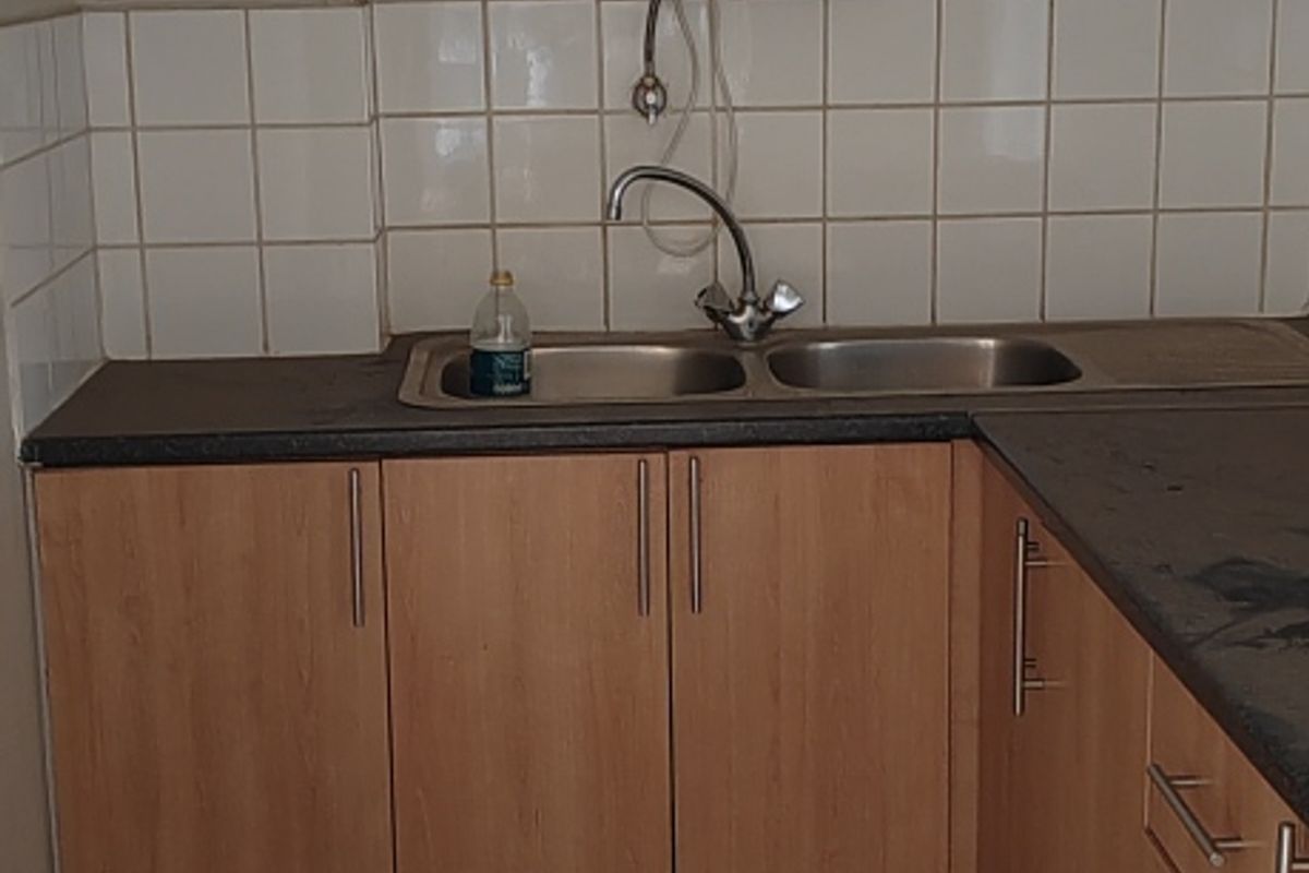 A functional kitchenette area featuring laminate cabinetry, a double sink, tiled backsplash, and an instant hot water dispenser.