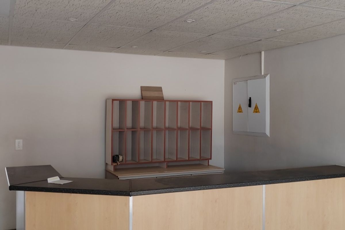 An industrial office space featuring a built-in reception counter, pigeonhole shelving, and a wall-mounted electrical distribution board under a suspended ceiling.