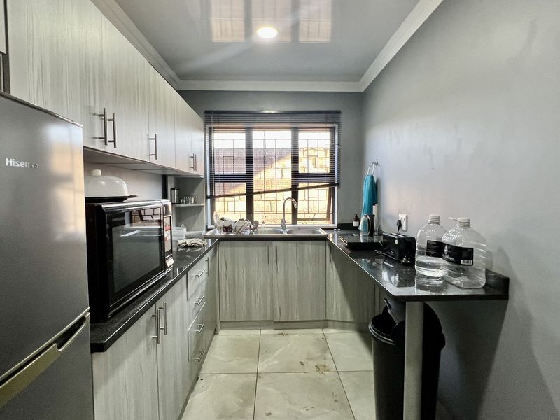 Compact kitchen featuring modern grey cabinetry, granite countertops, stainless steel sink, and tiled flooring with security bars on the window.