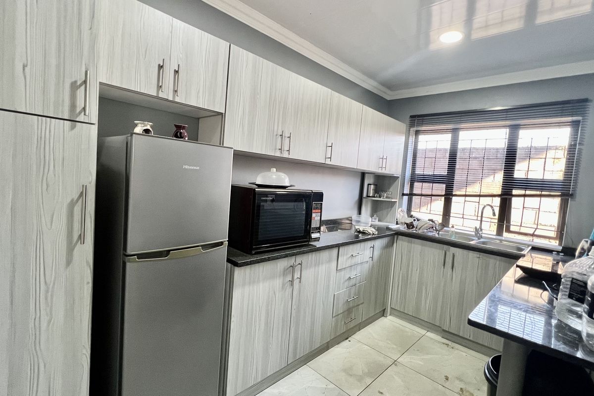 Modern kitchen featuring light wood-grain cabinetry, dark laminate countertops, stainless steel sink, and tiled flooring with natural light from the window.