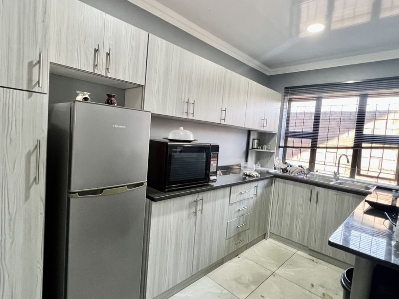 Modern kitchen featuring light wood-grain cabinetry, dark laminate countertops, stainless steel sink, and tiled flooring with natural light from the window.