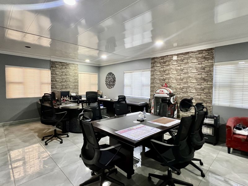 A spacious office area featuring glossy ceiling panels, stone veneer accent walls, and polished porcelain floor tiles with integrated venetian blinds.