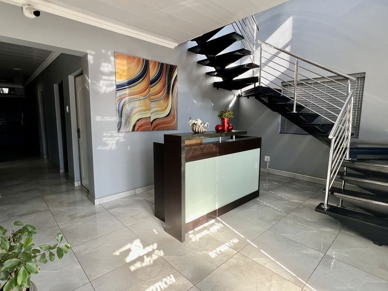 Modern industrial-style entrance foyer featuring a sleek reception desk, polished porcelain floor tiles, and a striking floating staircase with stainless steel railings.