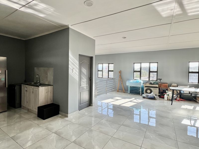 Spacious open-plan industrial area featuring polished tiled flooring, recessed lighting, and a functional kitchenette corner with modern cabinetry.