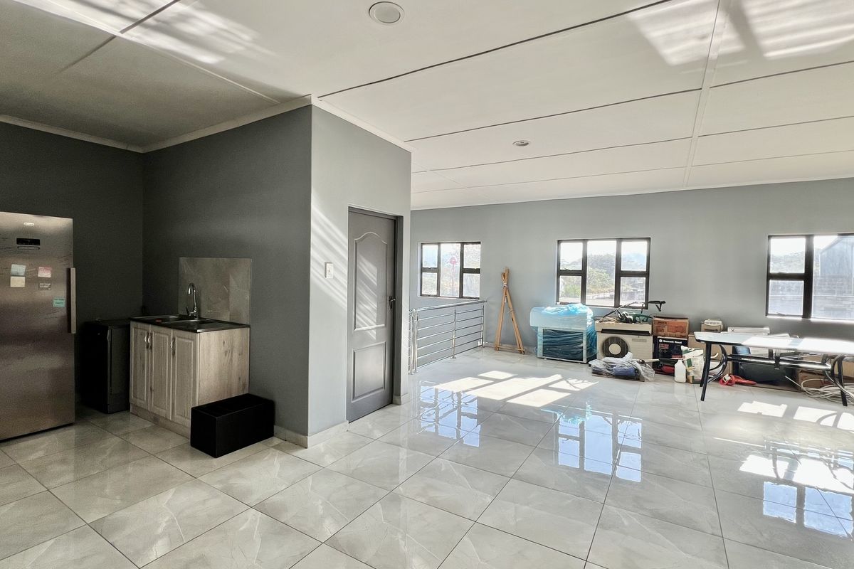 Spacious open-plan industrial area featuring polished tiled flooring, recessed lighting, and a functional kitchenette corner with modern cabinetry.
