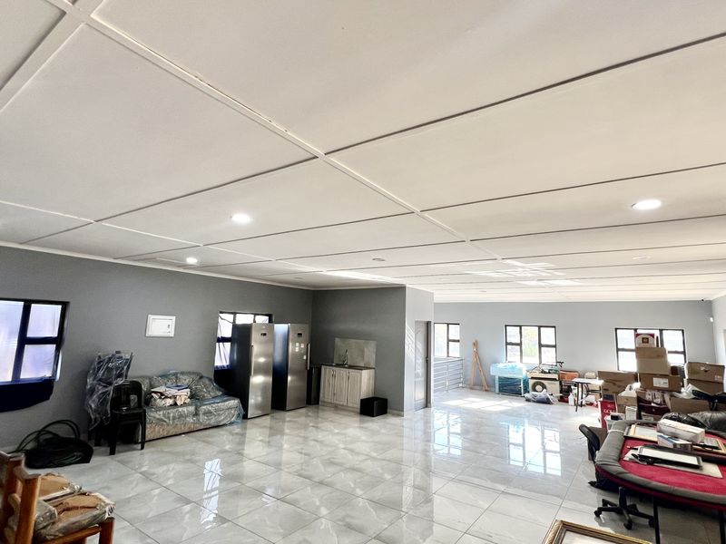 Spacious open-plan industrial area featuring polished tiled flooring, recessed lighting, and a compact kitchenette unit, suitable for versatile commercial or office use.