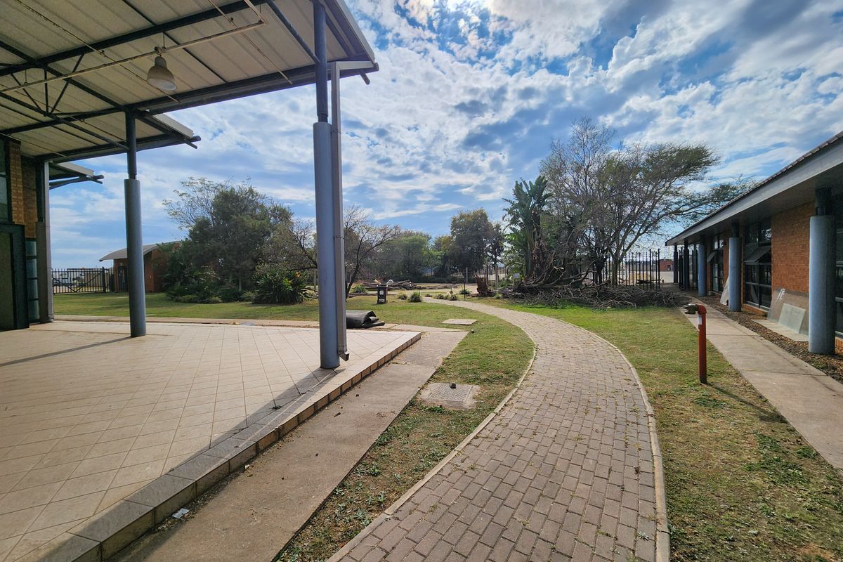 Spacious industrial outdoor area featuring a covered patio, paved walkways, and established garden space between building wings.