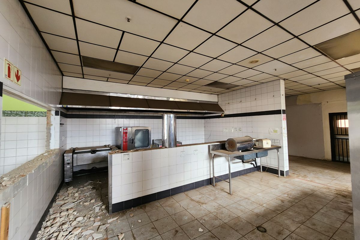 Industrial kitchen space featuring tiled surfaces, stainless steel extraction, and a service hatch, currently in need of refurbishment and repairs.