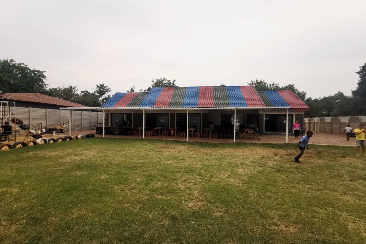 Exterior view of a commercial building featuring a multi-colored tiled roof, a covered patio area, and an expansive lawn.