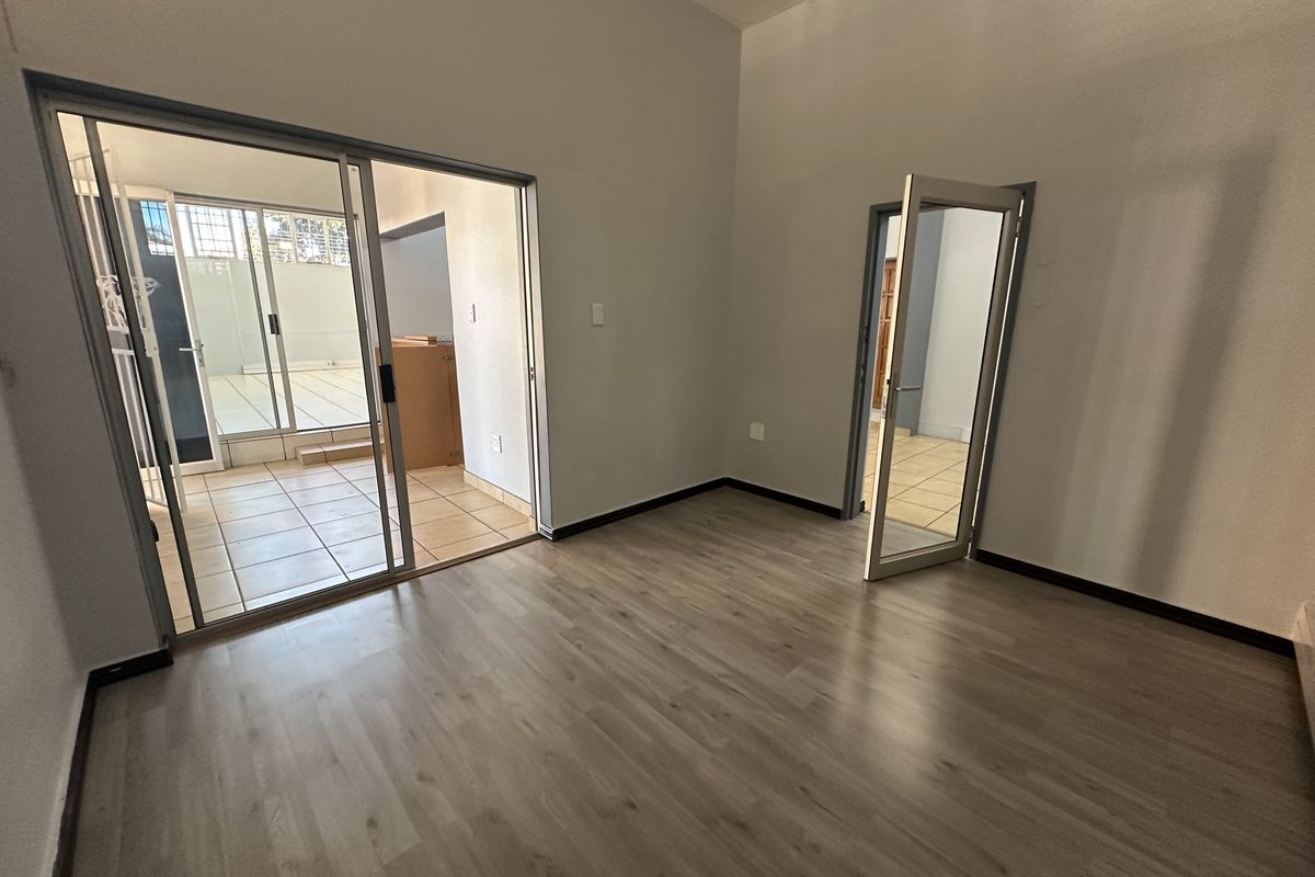 Spacious, empty living area featuring modern laminate flooring, neutral walls, and direct access to an adjacent tiled patio through sliding glass doors.