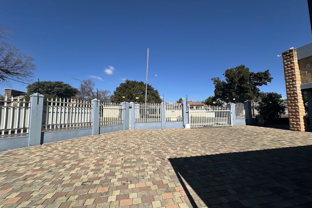 Front exterior view of the industrial property featuring a paved driveway, secure perimeter fencing with electric wires, and a sliding gate entrance.