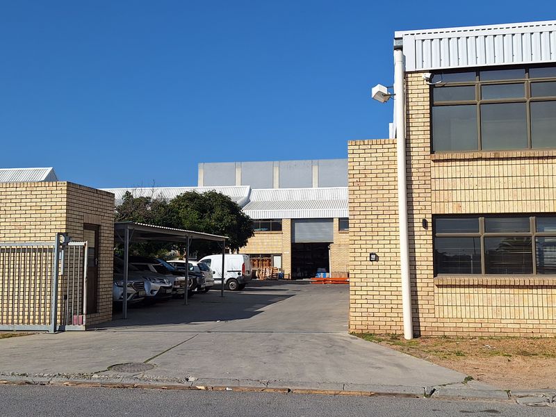 Front view of a commercial property featuring a brick facade, metal roofing, a gated entrance, and a paved driveway with an integrated carport.