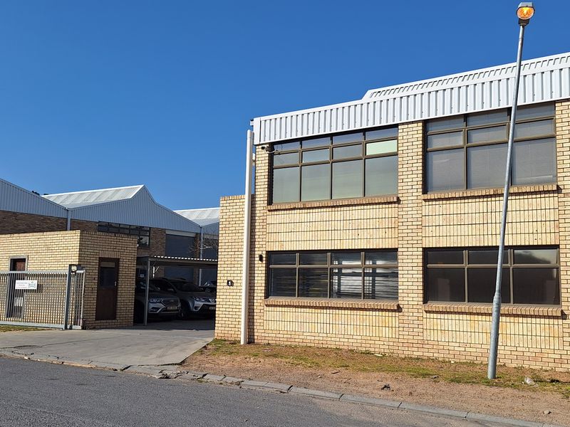 Front exterior view of a commercial face brick building featuring a secure gated entrance, paved driveway, and metal roofing.