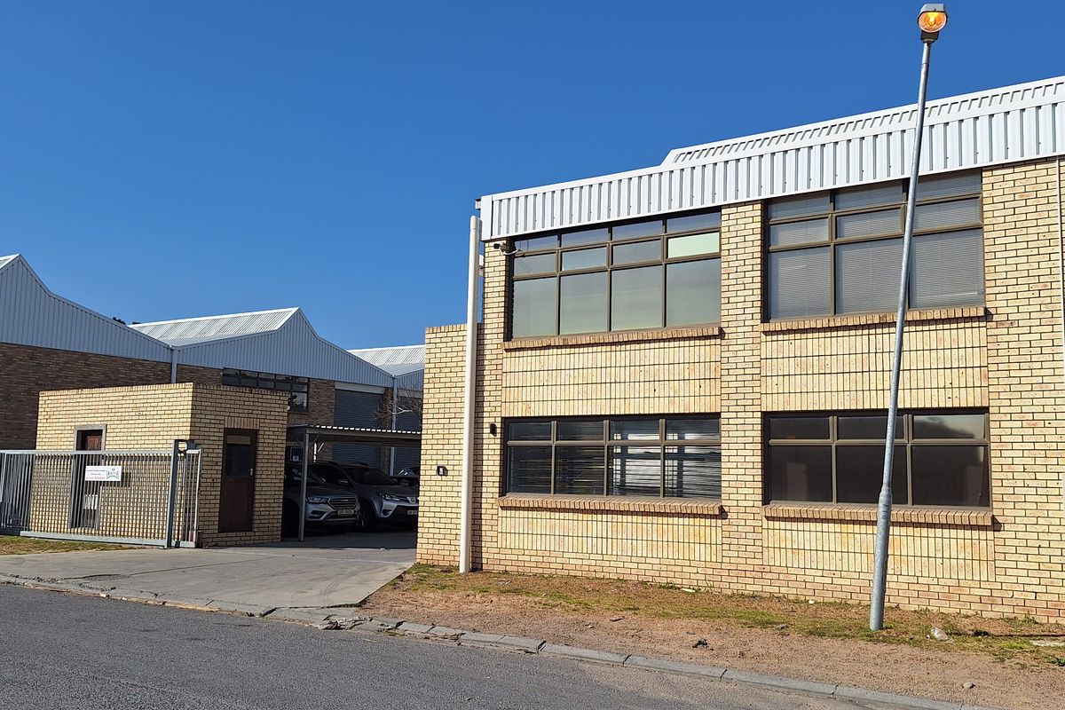 Front exterior view of a commercial face brick building featuring a secure gated entrance, paved driveway, and metal roofing.