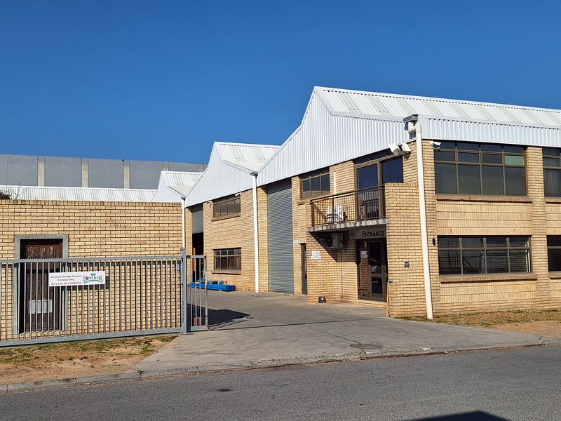 Front elevation of a commercial industrial property featuring face brick construction, metal roofing, secure gated access, and roller shutter doors.