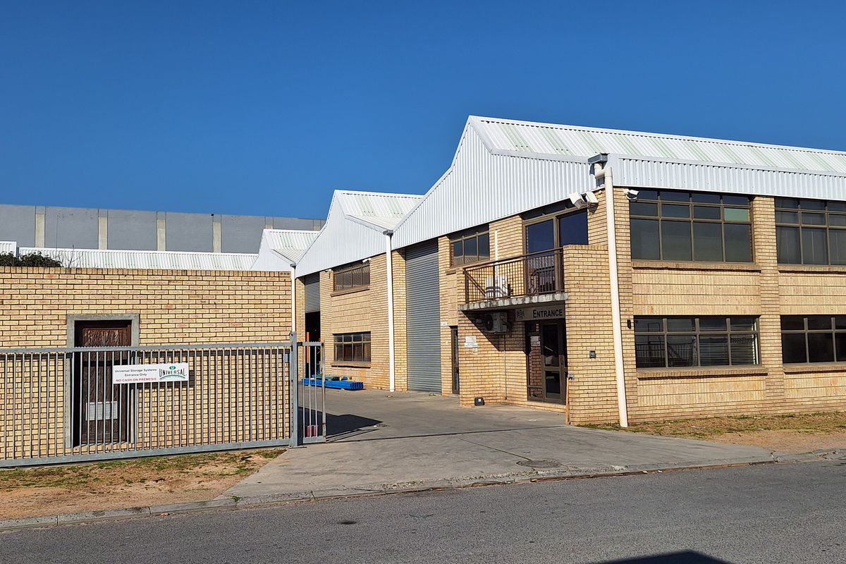 Front elevation of a commercial industrial property featuring face brick construction, metal roofing, secure gated access, and roller shutter doors.