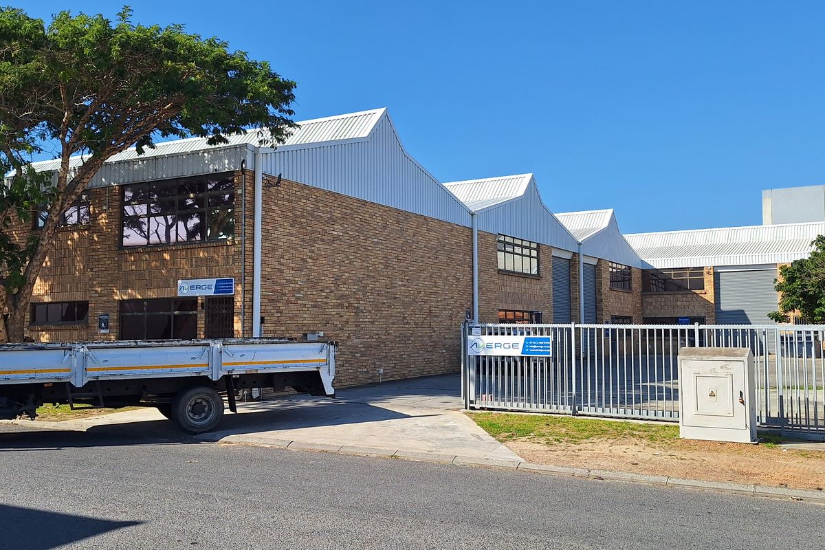 Front exterior view of a commercial industrial property featuring face brick construction, corrugated metal roofing, and secure gated access.