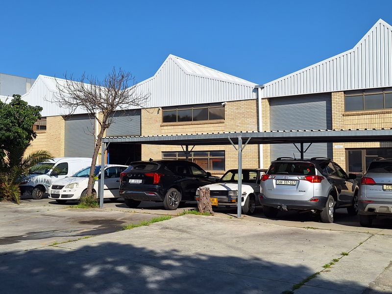 Front exterior view of a commercial industrial property featuring face brick facade, corrugated metal roofing, roller shutter doors, and a covered parking area.
