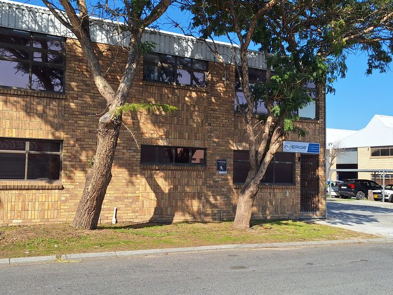 Front elevation of a commercial face brick building featuring aluminium windows, a roller shutter door, and secure gated access to the paved driveway.